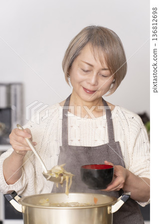一位老婦人在廚房裡熬豬肉湯,並用碗盛出來。 一位老婦人在廚房裡熬豬肉湯,並用碗盛出來。 136812698