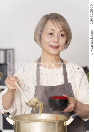 一位老婦人在廚房裡熬豬肉湯,並用碗盛出來。 一位老婦人在廚房裡熬豬肉湯,並用碗盛出來。 136812699