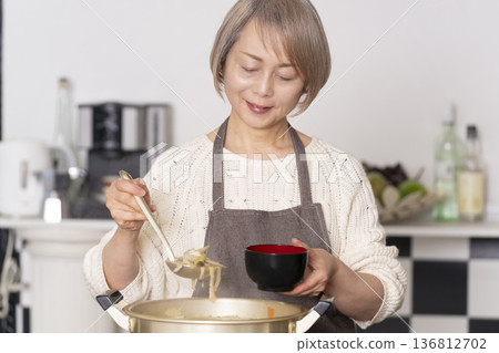 A senior woman making pork soup in the kitchen and serving it in a bowl A senior woman making pork soup in the kitchen and serving it in a bowl 136812702