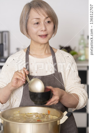 A senior woman making pork soup in the kitchen and serving it in a bowl A senior woman making pork soup in the kitchen and serving it in a bowl 136812707