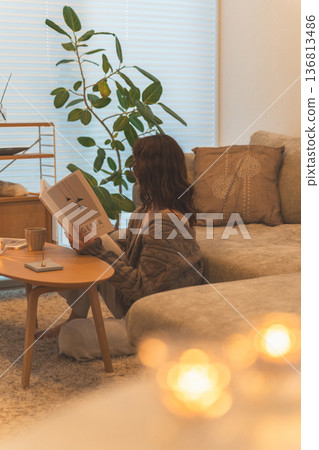 一位穿著時尚的亞洲女性坐在客廳閱讀雜誌。 136813486