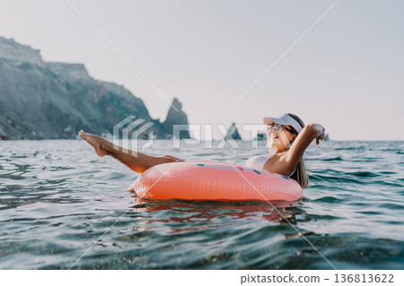 Woman, floating, ocean. Young woman relaxing on an inflatable donut in the calm sea during summer vacation with copy space. Woman, floating, ocean. Young woman relaxing on an inflatable donut in the calm sea during summer vacation with copy space. 136813622