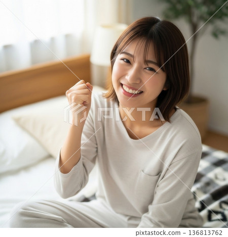 A young woman smiling and pumping her fist in her bedroom A young woman smiling and pumping her fist in her bedroom 136813762