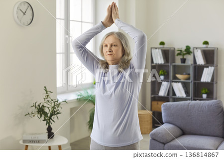 Healthy home yoga workout, meditation of senior woman, standing with hands up in namaste gesture Healthy home yoga workout, meditation of senior woman, standing with hands up in namaste gesture 136814867