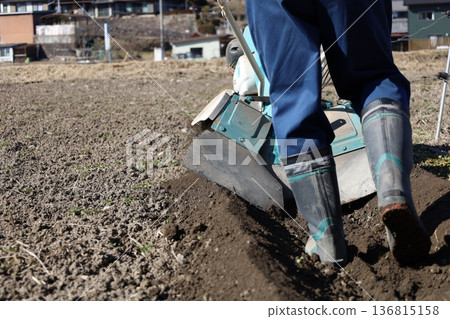 Close-up of a farmer's feet and a cultivator plowing the field. Agricultural scenery in Japan. Close-up of a farmer's feet and a cultivator plowing the field. Agricultural scenery in Japan. 136815158