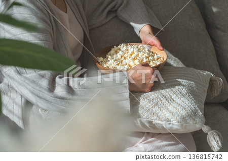 Hands of a woman sitting on a sofa and eating popcorn 136815742
