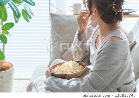 Woman sitting on sofa eating popcorn 136815743
