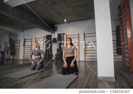 Women train together in gym while practicing yoga and exercising on mats Women train together in gym while practicing yoga and exercising on mats 136816107