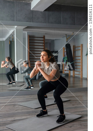 Woman practicing squats in gym during workout session with focus on fitness routine and group training 136816111