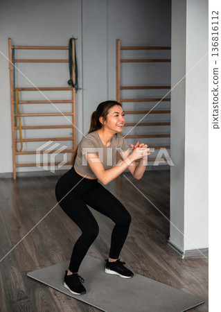 Fitness training session in gym with woman doing squats on exercise mat in morning light 136816112