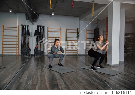 Women workout in gym doing squats on mats during morning training session for fitness Women workout in gym doing squats on mats during morning training session for fitness 136816114