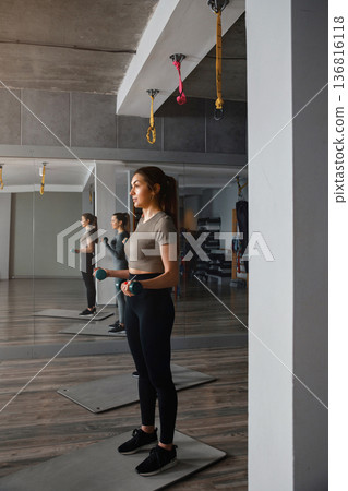 Woman stands with weights in gym during workout session in modern fitness studio Woman stands with weights in gym during workout session in modern fitness studio 136816118