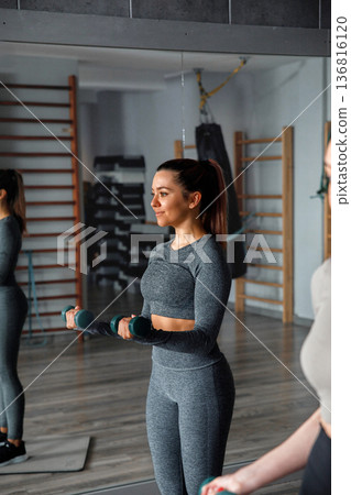 Woman works out with dumbbells in gym during fitness training session in the morning Woman works out with dumbbells in gym during fitness training session in the morning 136816120