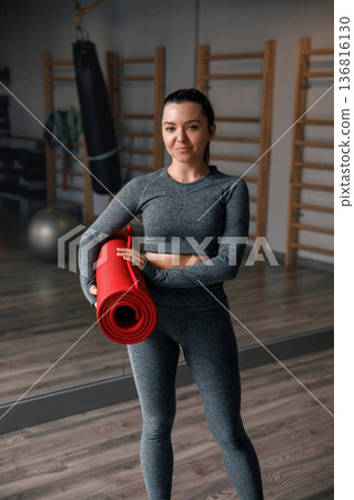 Woman holds a red yoga mat in a gym ready for her workout session in the morning Woman holds a red yoga mat in a gym ready for her workout session in the morning 136816130