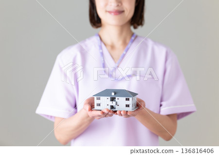 A middle-aged female nurse wearing a medical scrub holding a house model 136816406