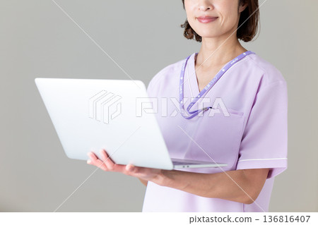 A middle-aged female nurse wearing a medical scrub with a laptop A middle-aged female nurse wearing a medical scrub with a laptop 136816407