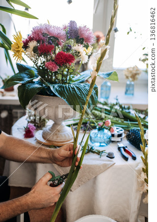 Hands of man use garden pruners to trim tall gladiolus stem on table. Artisanal floral design, skilled hands, master craftsman at work, creative professional, niche hobby. Hands of man use garden pruners to trim tall gladiolus stem on table. Artisanal floral design, skilled hands, master craftsman at work, creative professional, niche hobby. 136816462