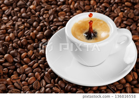 Small white espresso cup with splash and drop, brimming with aromatic coffee resting on bed of roasted beans Small white espresso cup with splash and drop, brimming with aromatic coffee resting on bed of roasted beans 136816558