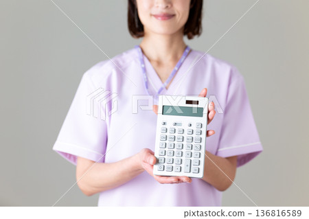 一位身穿醫用工作服的中年女護士，手裡拿著計算器 136816589