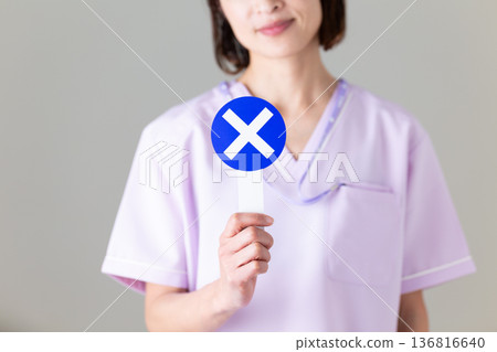 A middle-aged female nurse wearing a medical scrub holding a cross plate A middle-aged female nurse wearing a medical scrub holding a cross plate 136816640