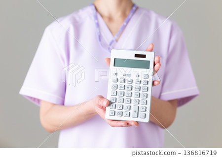 一位身穿醫用工作服的中年女護士,手裡拿著計算器 一位身穿醫用工作服的中年女護士,手裡拿著計算器 136816719