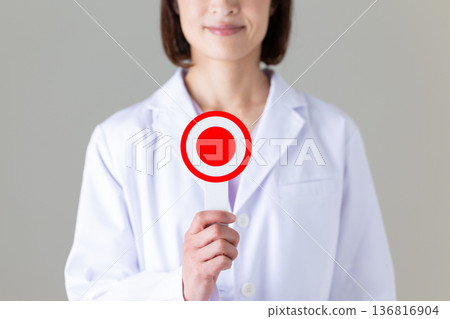 一位身穿白大褂的中年女醫生，手裡拿著一個圓盤。 136816904