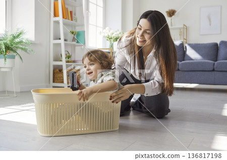 Mother, babysitter, little child playing funny basket race pushing game at table together, mom 136817198