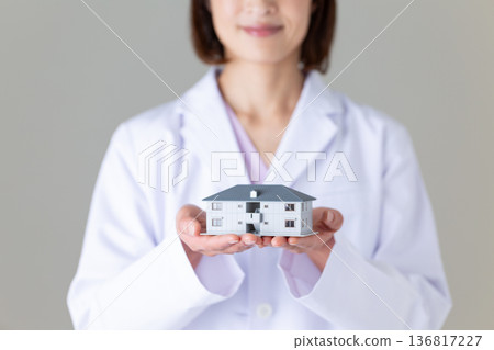 一位身穿白大褂的中年女醫生,手裡拿著一個房屋模型。 一位身穿白大褂的中年女醫生,手裡拿著一個房屋模型。 136817227