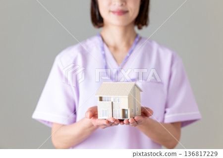 A middle-aged female nurse wearing a medical scrub holding a house model A middle-aged female nurse wearing a medical scrub holding a house model 136817229