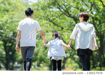 Rear view of a family walking in a park with fresh green leaves 136817439