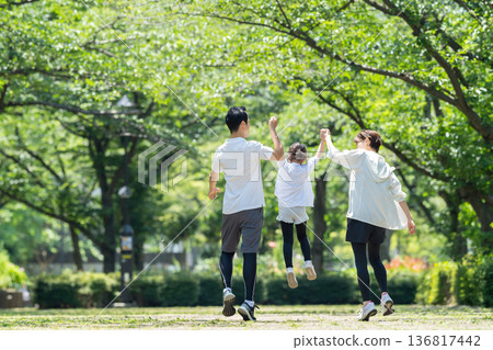 Rear view of a family walking in a park with fresh green leaves Rear view of a family walking in a park with fresh green leaves 136817442