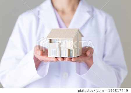 一位身穿白大褂的中年女醫生，手裡拿著一個房屋模型。 136817449