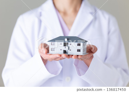 一位身穿白大褂的中年女醫生，手裡拿著一個房屋模型。 136817450