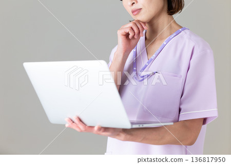 A middle-aged female nurse in a medical scrub looking at a laptop computer and worrying 136817950