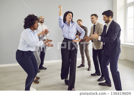 Company employees celebrating success congratulating female colleague indoors. Company employees celebrating success congratulating female colleague indoors. 136819609