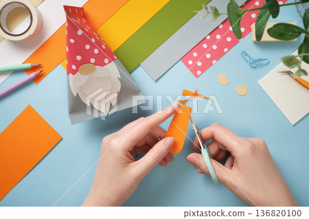 Hands cut carrots out of orange paper. Colorful paper, scissors, tape on blue background. DIY handmade art project for kids. Hands cut carrots out of orange paper. Colorful paper, scissors, tape on blue background. DIY handmade art project for kids. 136820100