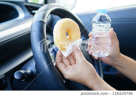 Bangkok, Thailand March 16, 2025 Asian woman driver hold cold water and sandwich bread for eat and drink in car, dangerous and risk an accident. Bangkok, Thailand March 16, 2025 Asian woman driver hold cold water and sandwich bread for eat and drink in car, dangerous and risk an accident. 136820796