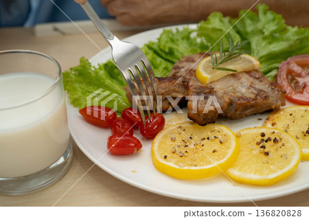 Asian elderly woman patient eating pork chop stake and vegetable salad for healthy food in hospital. 136820828
