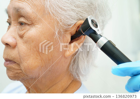 Otolaryngologist or ENT physician doctor examining senior patient ear with otoscope, hearing loss problem. 136820973