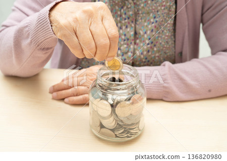 Retired elderly woman putting coins money in piggy bank and worry about monthly expenses and treatment fee payment. 136820980