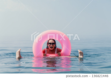 Woman ocean inflatable. A joyful woman enjoys a refreshing swim in the sea with a pink inflatable ring during a summer vacation Woman ocean inflatable. A joyful woman enjoys a refreshing swim in the sea with a pink inflatable ring during a summer vacation 136821446