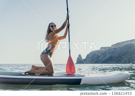 Woman Paddleboarding Ocean - A woman in a bikini poses on a paddleboard in the ocean. 136821453