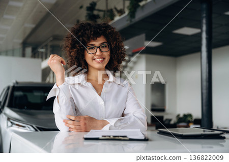 Sitting by the table with document. Female employee is in the car retail shop 136822009