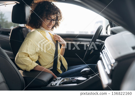 Fastens the seat belt. Happy woman is sitting in the car 136822160
