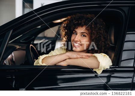 Looking through the opened window and smiling. Happy woman is sitting in the car 136822181