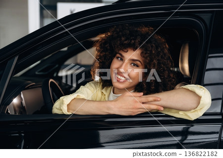 Looking through the opened window and smiling. Happy woman is sitting in the car 136822182