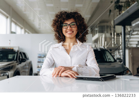 Sitting by the table with document. Female employee is in the car retail shop Sitting by the table with document. Female employee is in the car retail shop 136822233