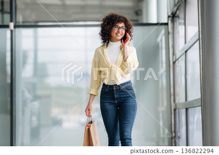 Conversation by using phone. Beautiful woman is standing indoors against blurred wall Conversation by using phone. Beautiful woman is standing indoors against blurred wall 136822294