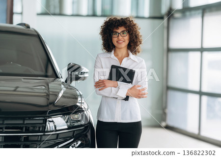 By the black vehicle. Female employee is in the car retail shop By the black vehicle. Female employee is in the car retail shop 136822302