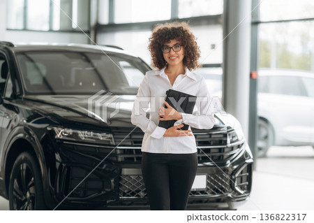 Front view, standing and holding digital tablet. Female employee is in the car retail shop 136822317